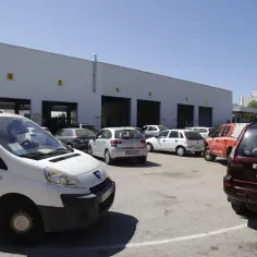 Furgoneta blanca y varios coches aparcados frente a un edificio con puertas de garaje numeradas.